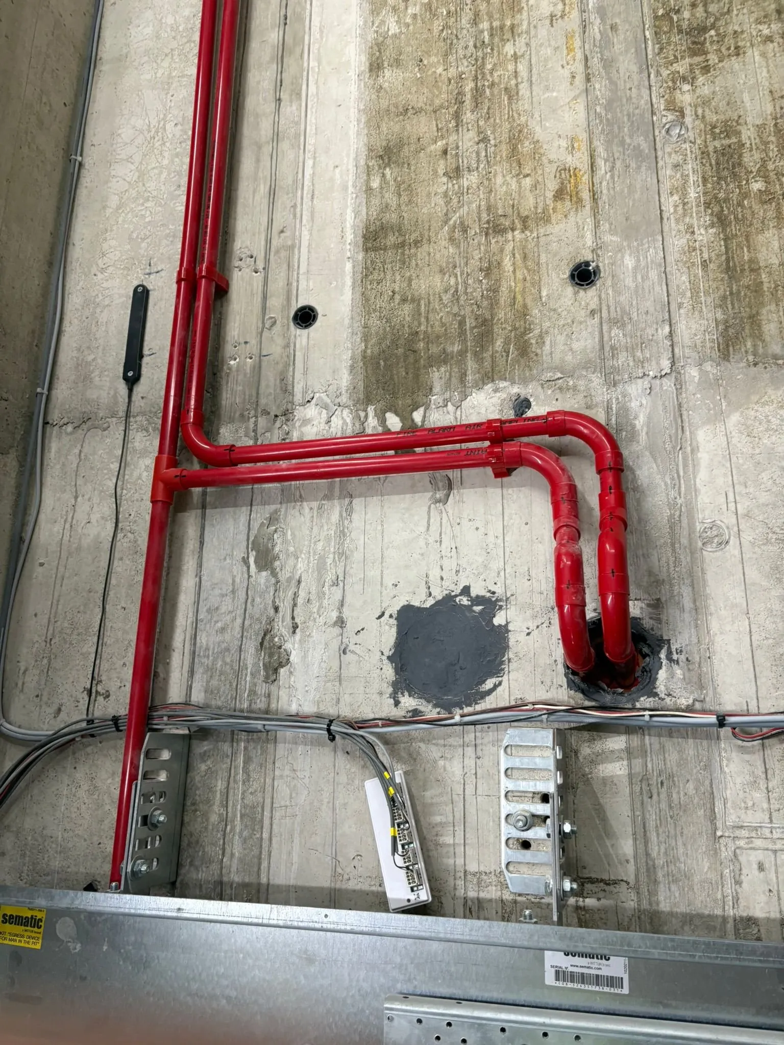 Neat red fire detection air-sampling pipework run cleanly across concrete.