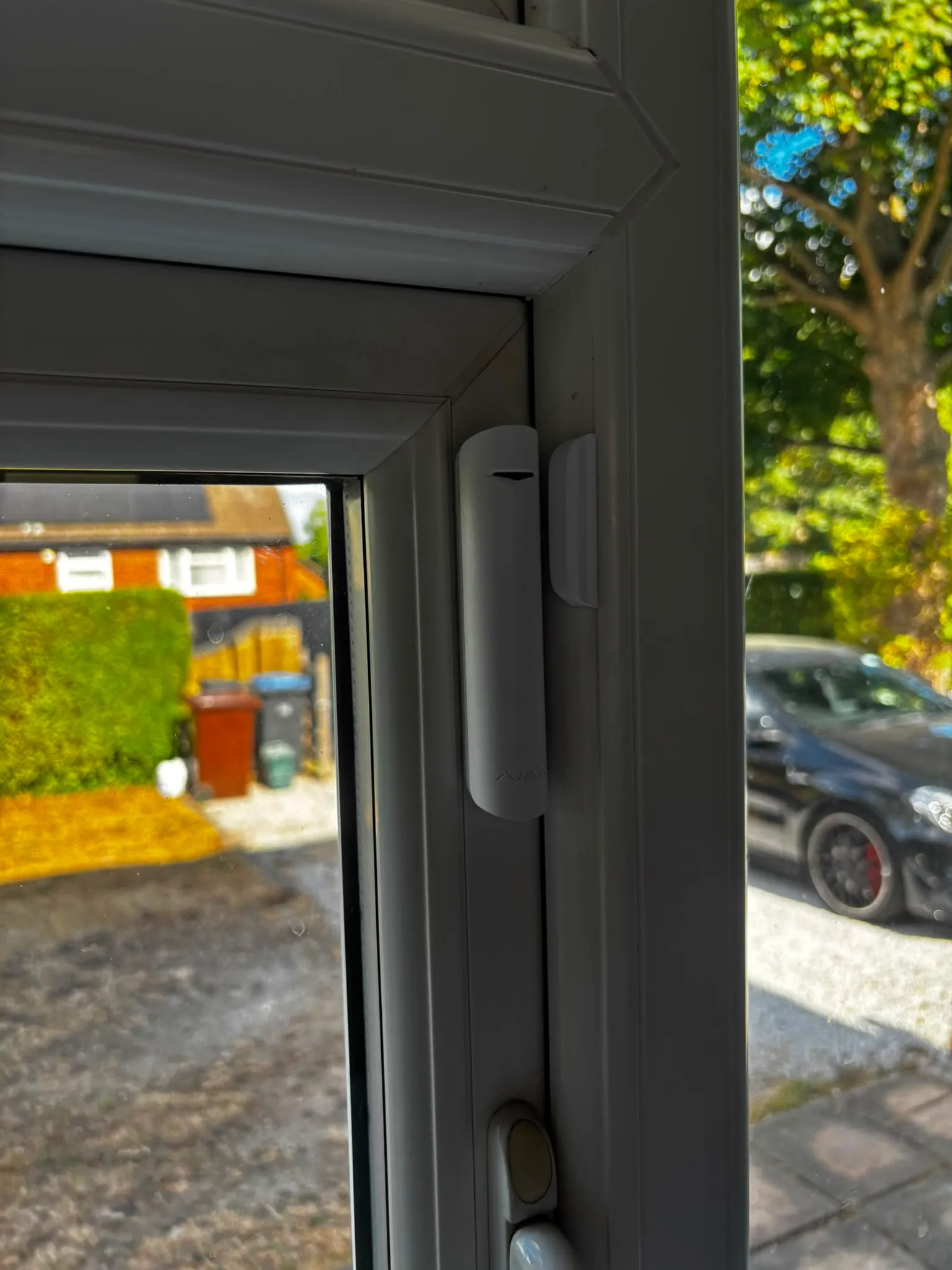 Ajax door contact fitted to a front door frame, aligned squarely with its magnet.