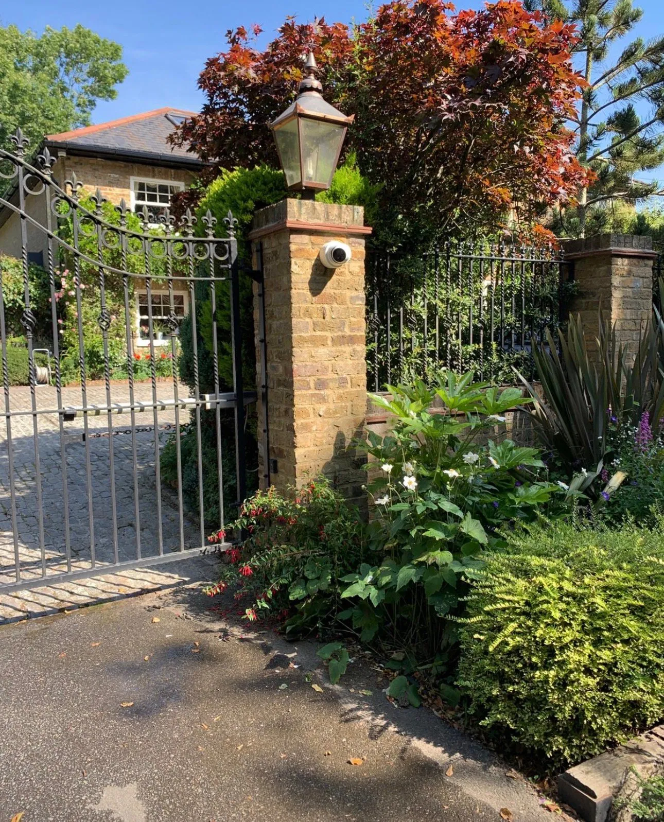 Ornate gate entrance with lamp post and lush garden landscaping.