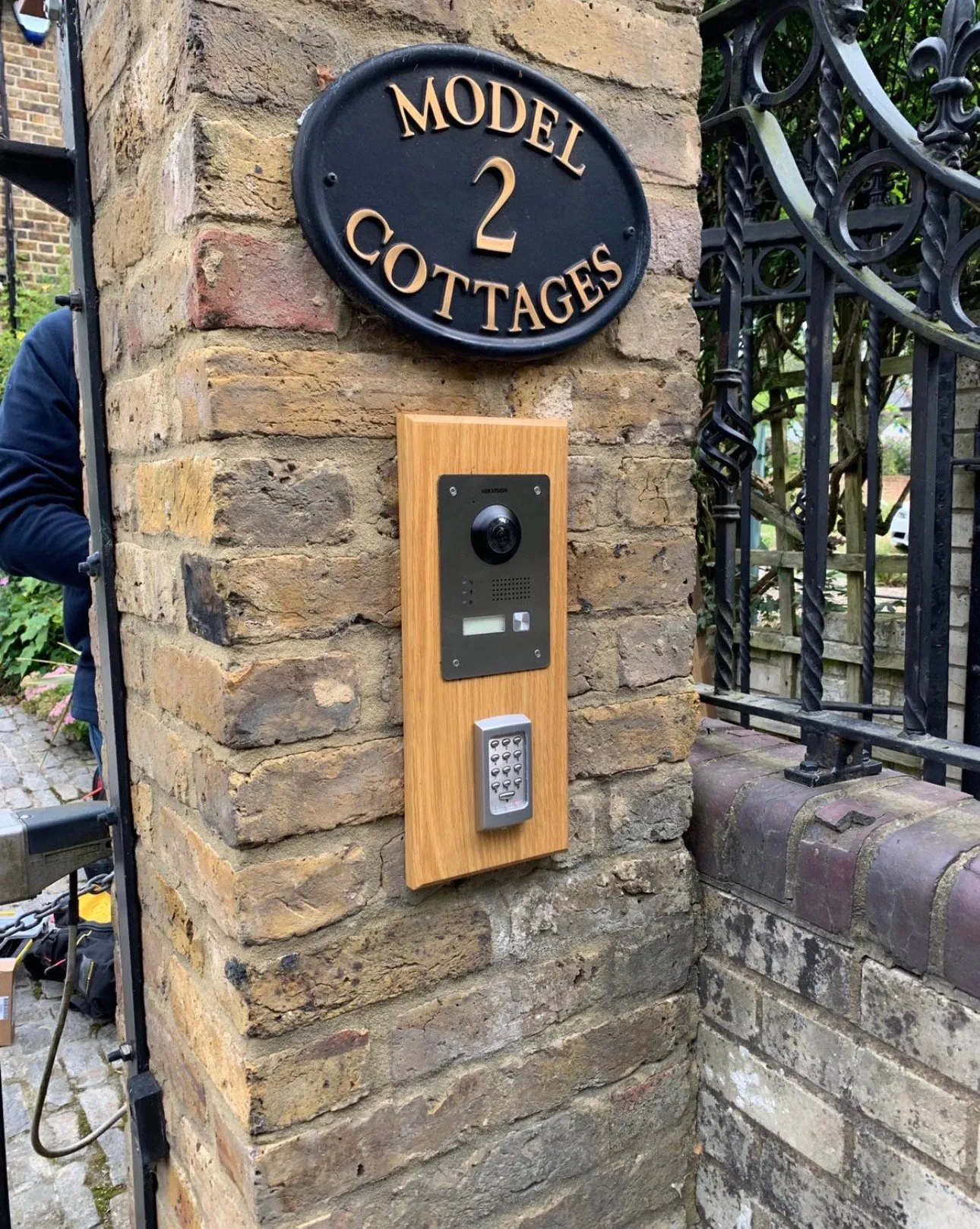 Video intercom with camera and keypad access control mounted on an oak entrance panel.