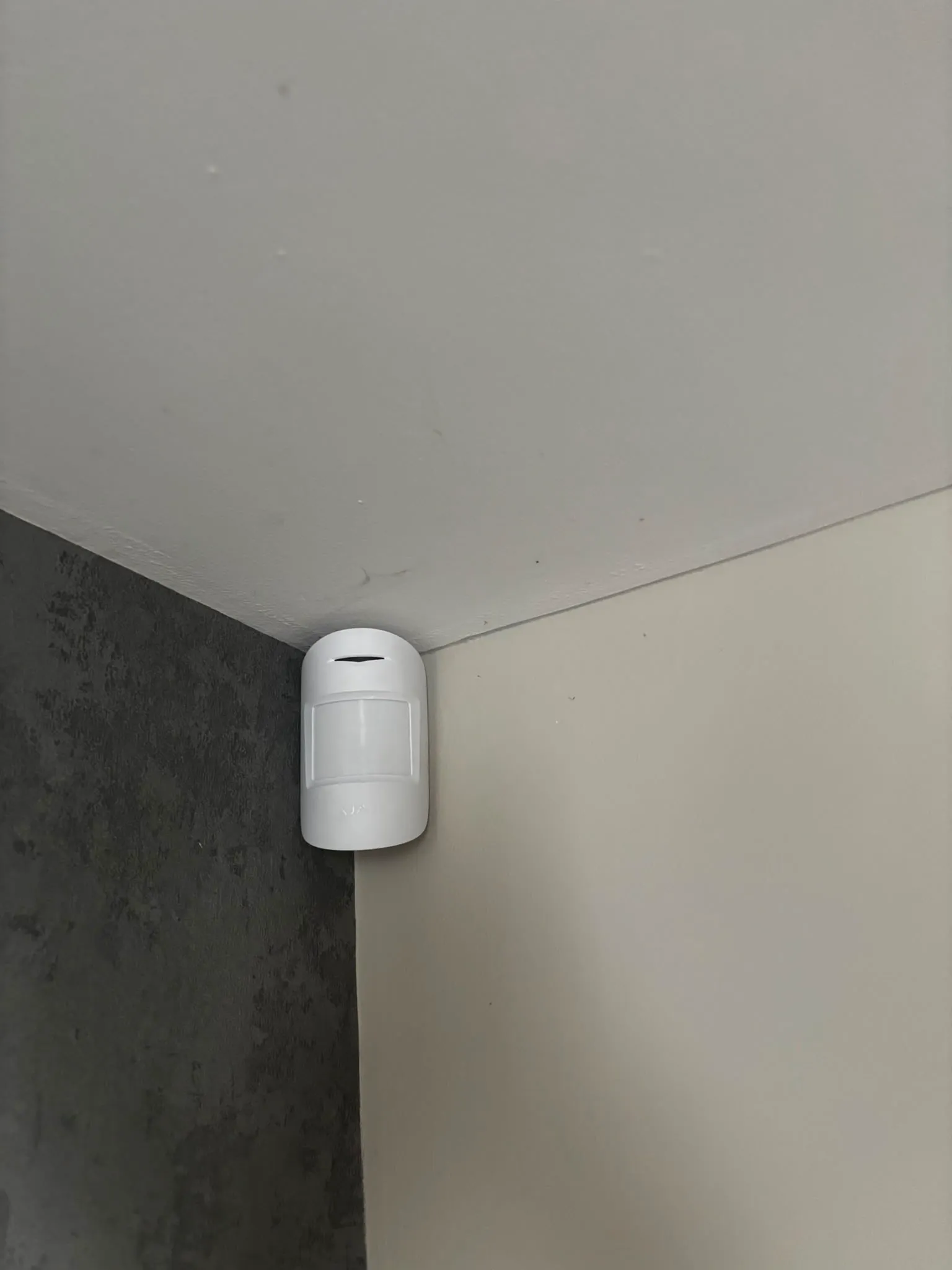 Ajax motion detector mounted in a room corner for full coverage without facing a window.