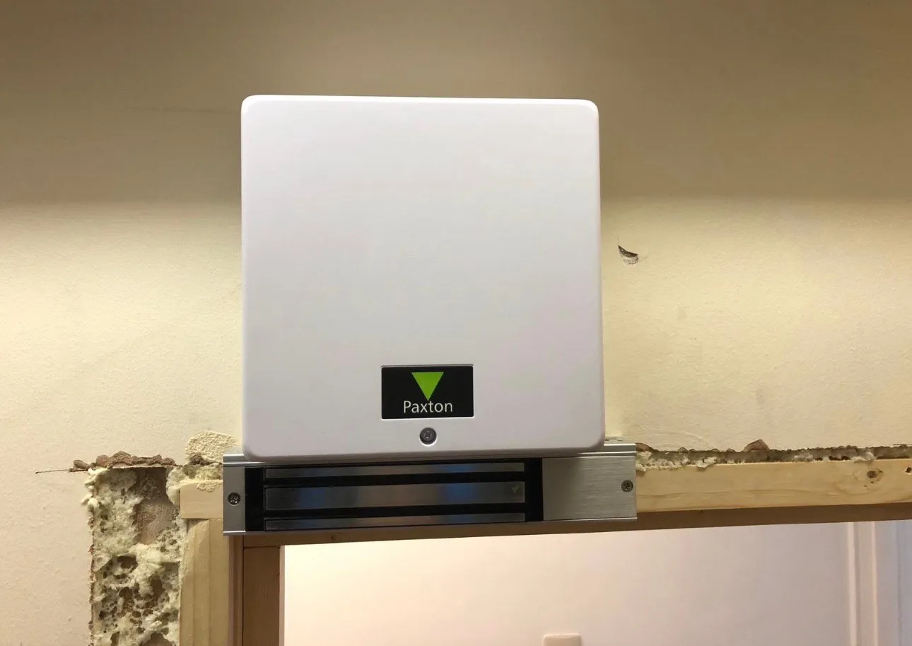 Paxton proximity access control unit fitted above a maglock at a commercial doorway.