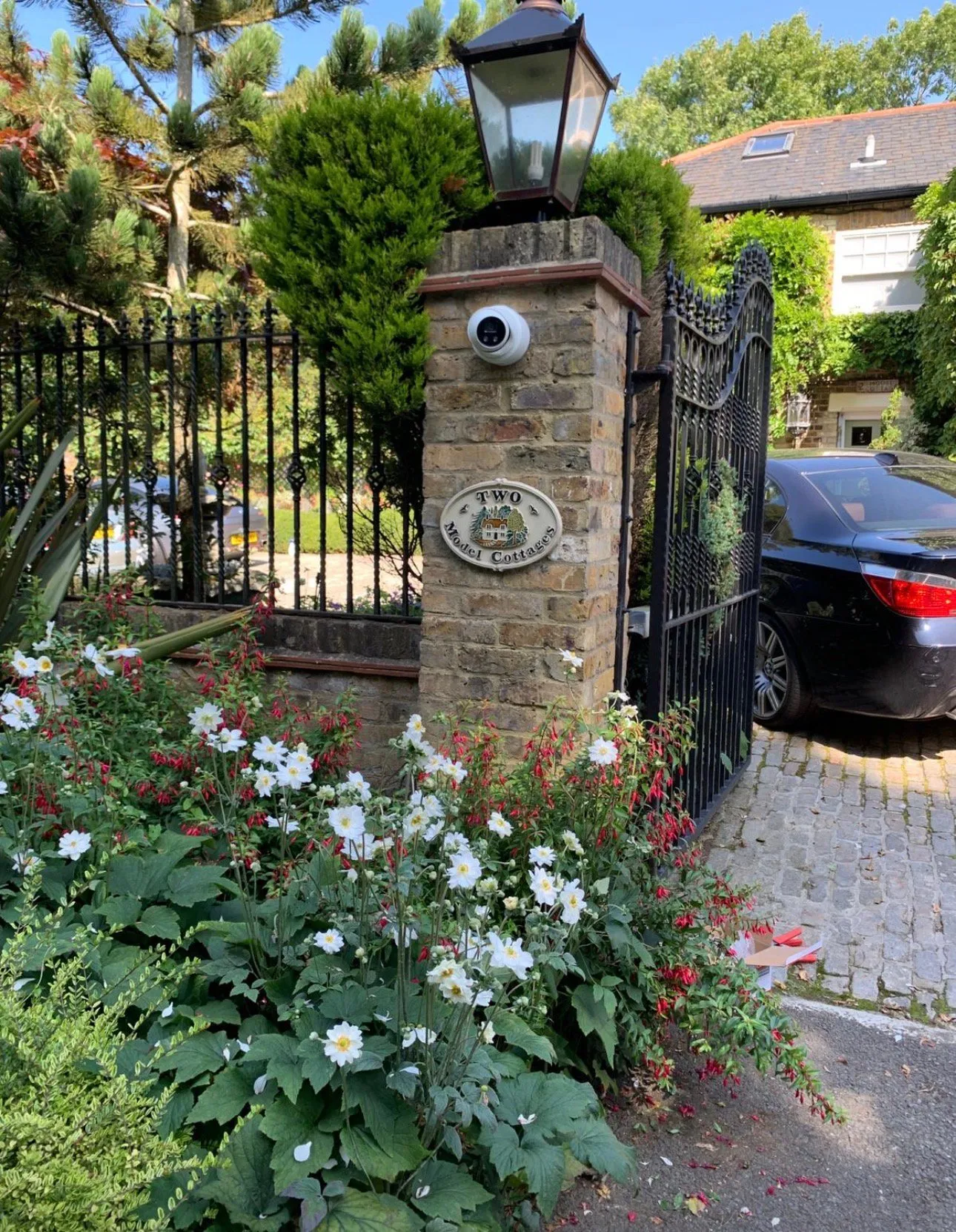 Dome camera mounted on stone pillar at property entrance with flowering borders.