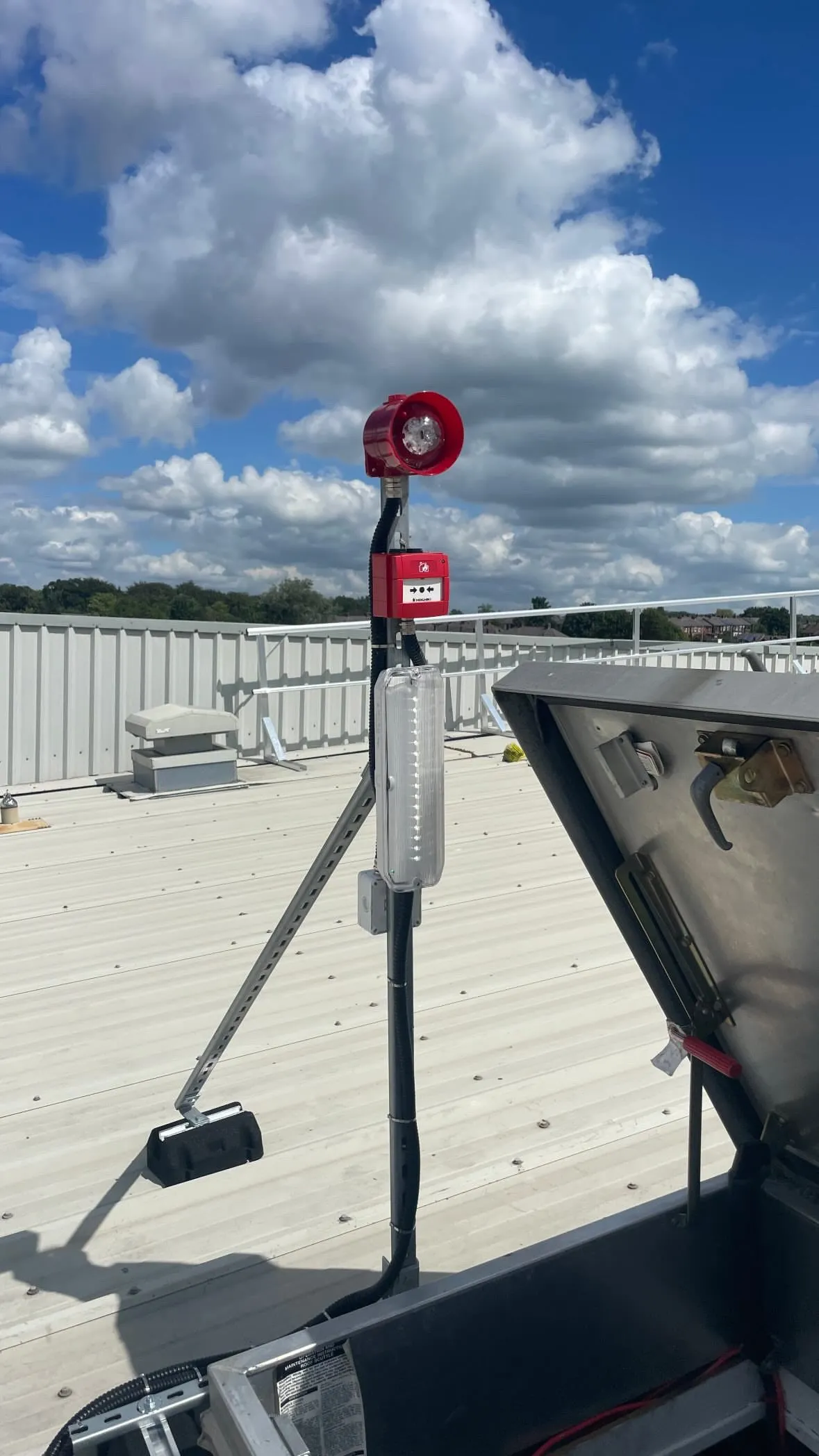 Emergency lighting, beacon and call point mounted at a rooftop escape hatch.