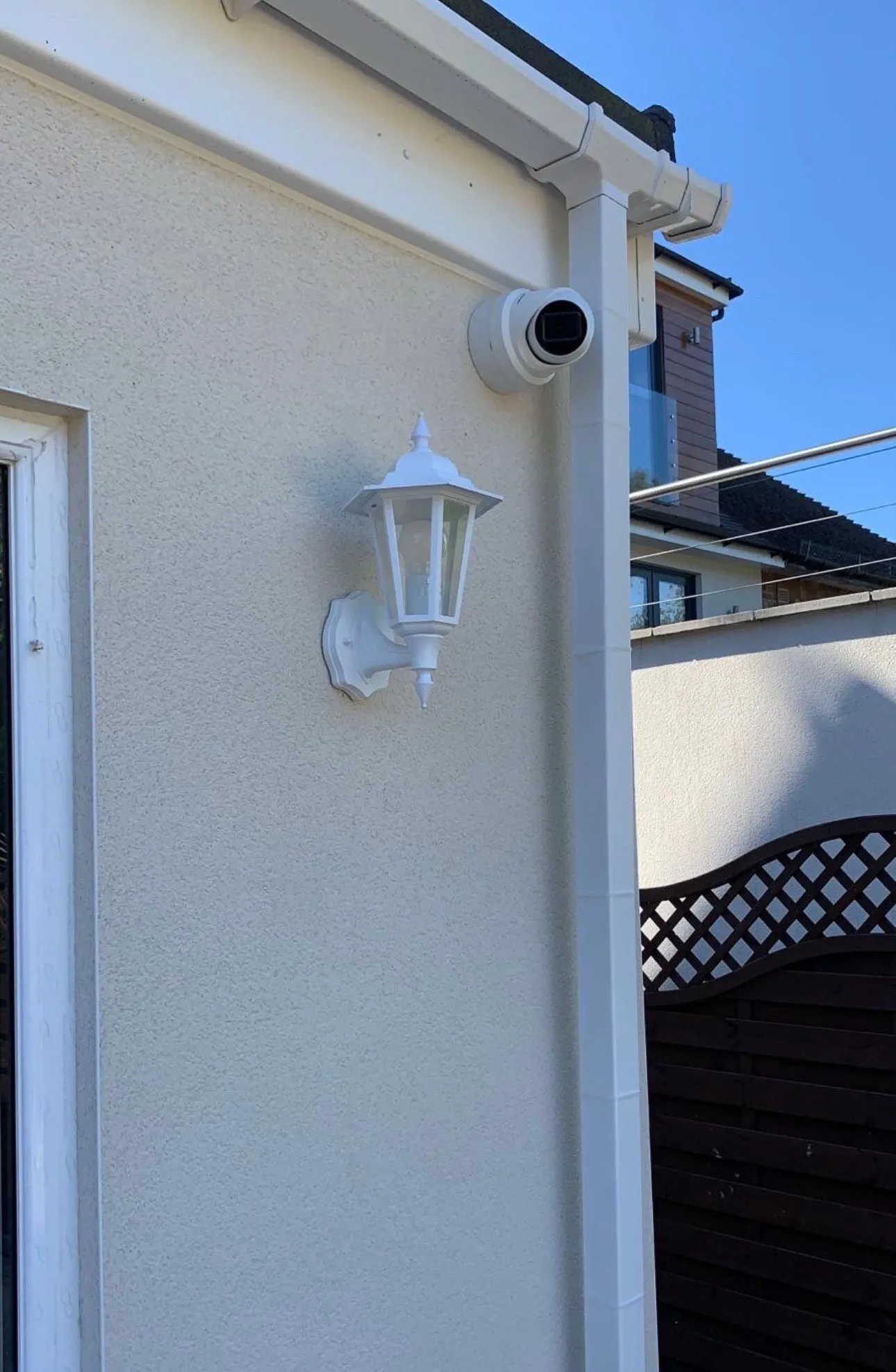 White dome camera mounted on building exterior with gutter and downpipe.